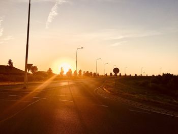 Sun streaming on empty road against sky during sunset