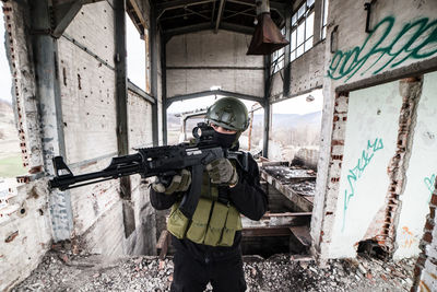 Army soldier aiming rifle while standing in building