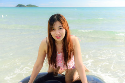 Portrait of young woman on inflatable ring at sea shore against sky