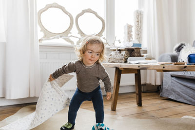 Baby girl holding rug while standing at home