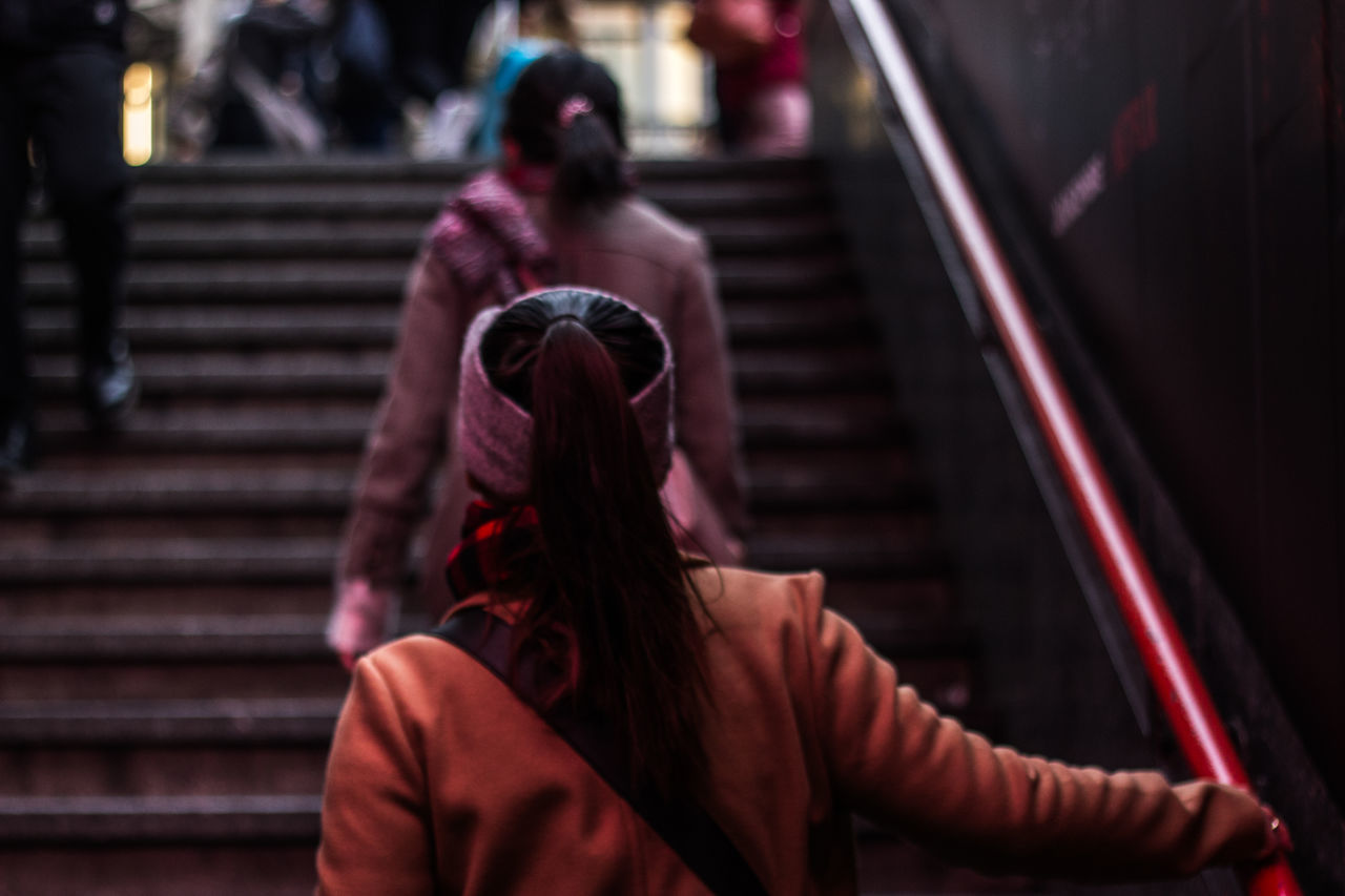 staircase, steps and staircases, real people, women, architecture, lifestyles, people, adult, focus on foreground, indoors, railing, leisure activity, sitting, rear view, incidental people, hairstyle, built structure, long hair, casual clothing, warm clothing