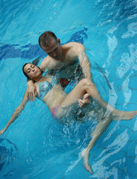 High angle view of mature man teaching young daughter swimming in pool