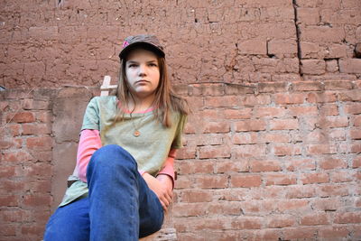 Portrait of teenage girl sitting against brick wall