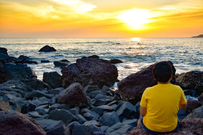 Rear view of boy looking at sea during sunset
