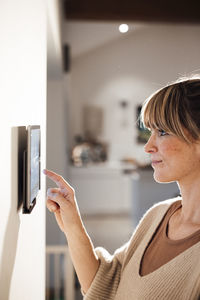 Woman touching tablet pc mounted on wall at home