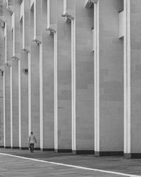 Man walking on footpath by historical concrete massive pattern lines building