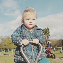 Cute girl looking away while sitting on seesaw against sky in playground