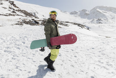 Smiling young man walking with snowboard on sunny day