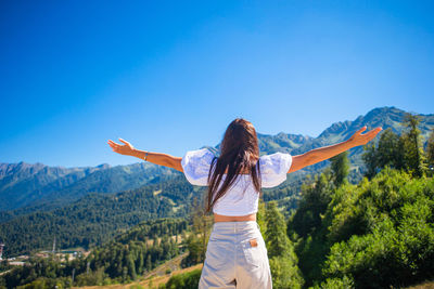 Rear view of woman standing on mountain against blue sky