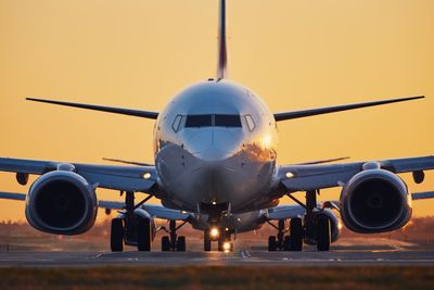 Airplane on airport runway against sky during sunset
