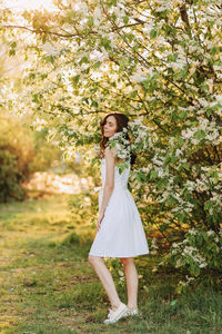 A cute happy young woman with a hairstyle in a white dress is walking enjoying nature in the summer