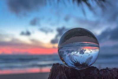 Close-up of crystal ball on rock against sea during sunset