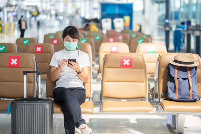 Woman wearing mask using phone sitting at airport
