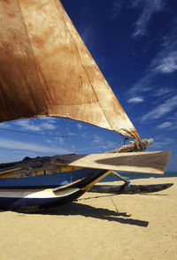 Outrigger boat moored at beach during sunny day