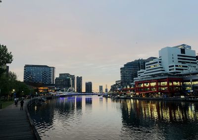 City buildings by river against sky during sunset