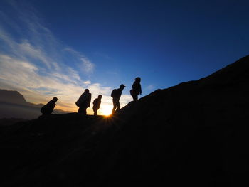 Silhouette people on rock against sky during sunset
