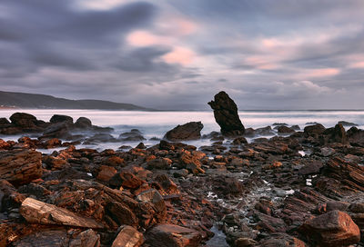 Rocks on beach against sky during sunset