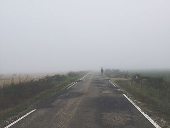 Road amidst fields against sky during foggy weather