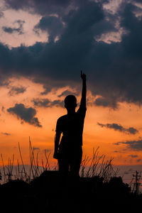 Silhouette woman with arms raised against sky during sunset