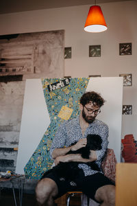 Full length of man sitting against illuminated wall at home