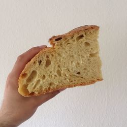 Cropped image of person hand holding bread against white wall