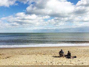 People sitting on beach by sea against sky