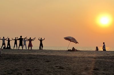 Silhouette people on beach against sky during sunset