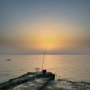 Fishing rod on rock by sea against sky during sunset