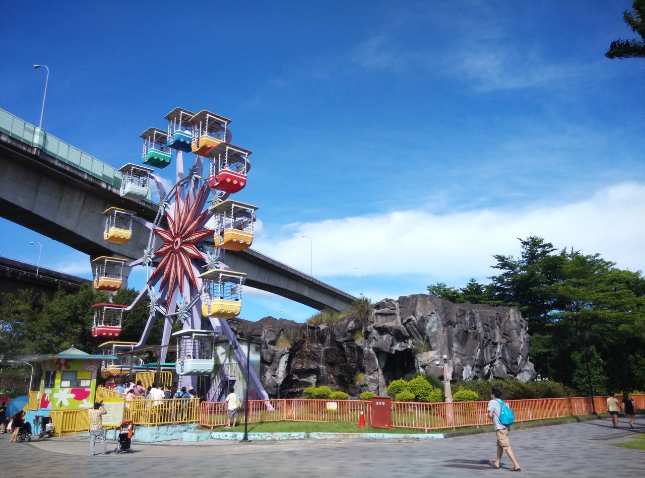 sky, leisure activity, lifestyles, men, person, built structure, large group of people, architecture, blue, arts culture and entertainment, amusement park, tourist, low angle view, cloud - sky, tourism, amusement park ride, tree, building exterior, group of people