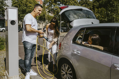 Father and mother with electric plug at gas station on sunny day