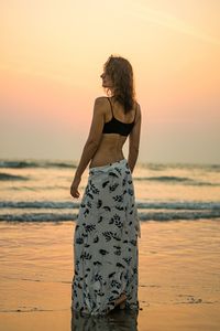 Woman standing at beach against sky during sunset