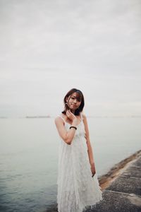 Portrait of young woman standing by sea against sky