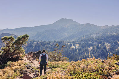 Rear view of man standing on mountain against clear sky