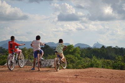 Rear view of man riding bicycle on field against sky