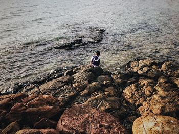 Man sitting on rock by sea