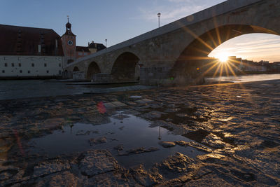 Arch bridge over river by buildings against sky during sunset