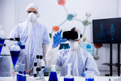 Scientist wearing virtual reality simulator colleague in background at laboratory