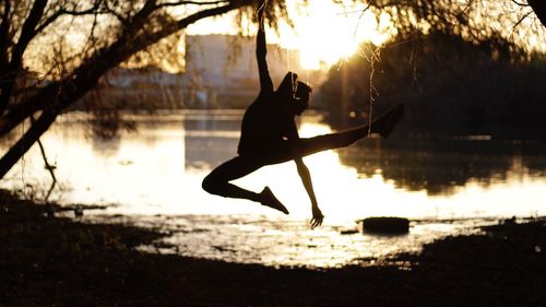 Silhouette man in lake against sky during sunset