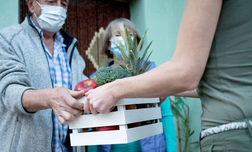 Midsection of woman giving crate to senior couple during pandemic