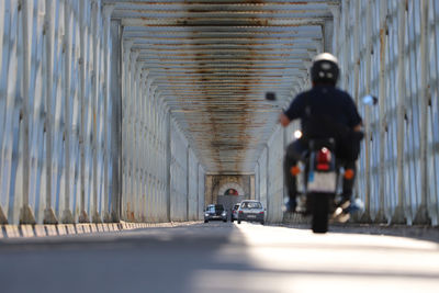 View of sunlit interior of metal bridge with motorcycle in foreground with illusion
