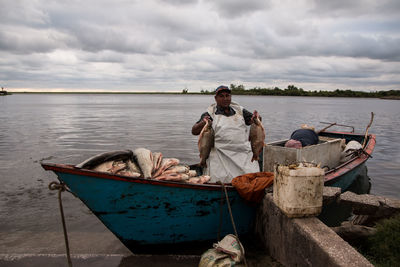 Portrait of man holding fish while sitting in boat on lake