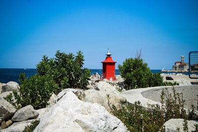 Lighthouse by sea against clear blue sky