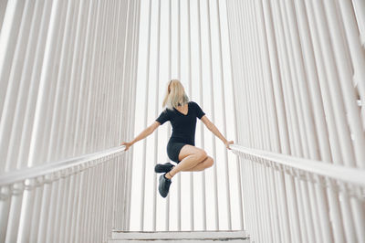 Low angle view of woman jumping while holding railings against architectural column