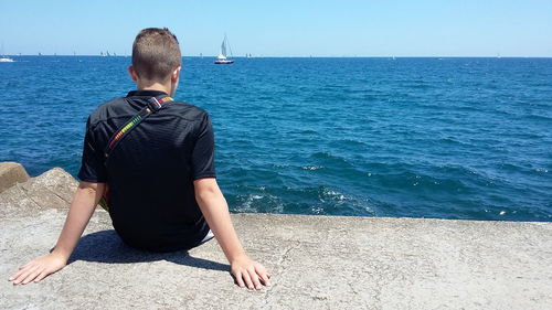 Rear view of man sitting in sea against clear sky