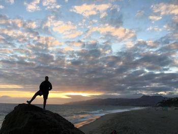 Man standing on rock by sea against sky during sunset