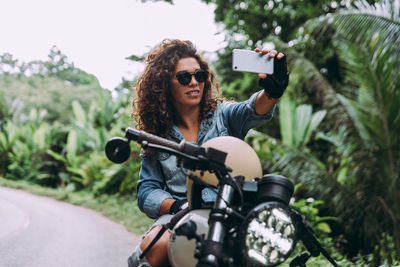 Portrait of woman taking selfie while sitting on motor cycle