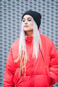 Portrait of beautiful young woman standing against red wall