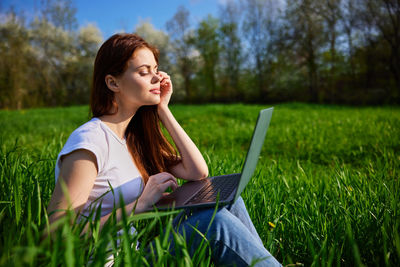 Young woman using laptop while sitting on field