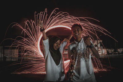 Happy friends standing against light painting at night