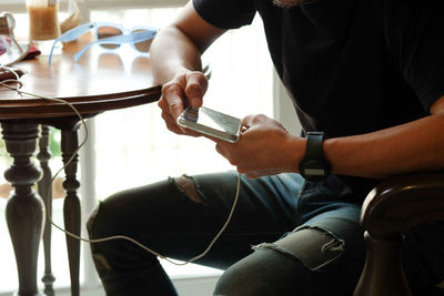 Midsection of man using smart phone while sitting on chair